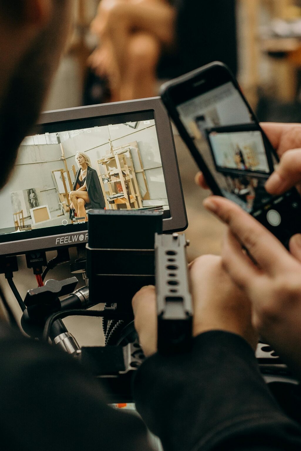 A photographer captures a video on a smartphone and monitor inside a studio setting.